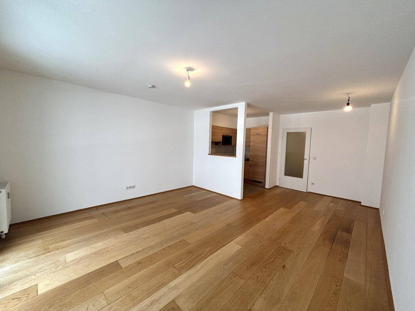 Geräumiger, leerer Wohnbereich mit Holzboden und Blick zur Küche.