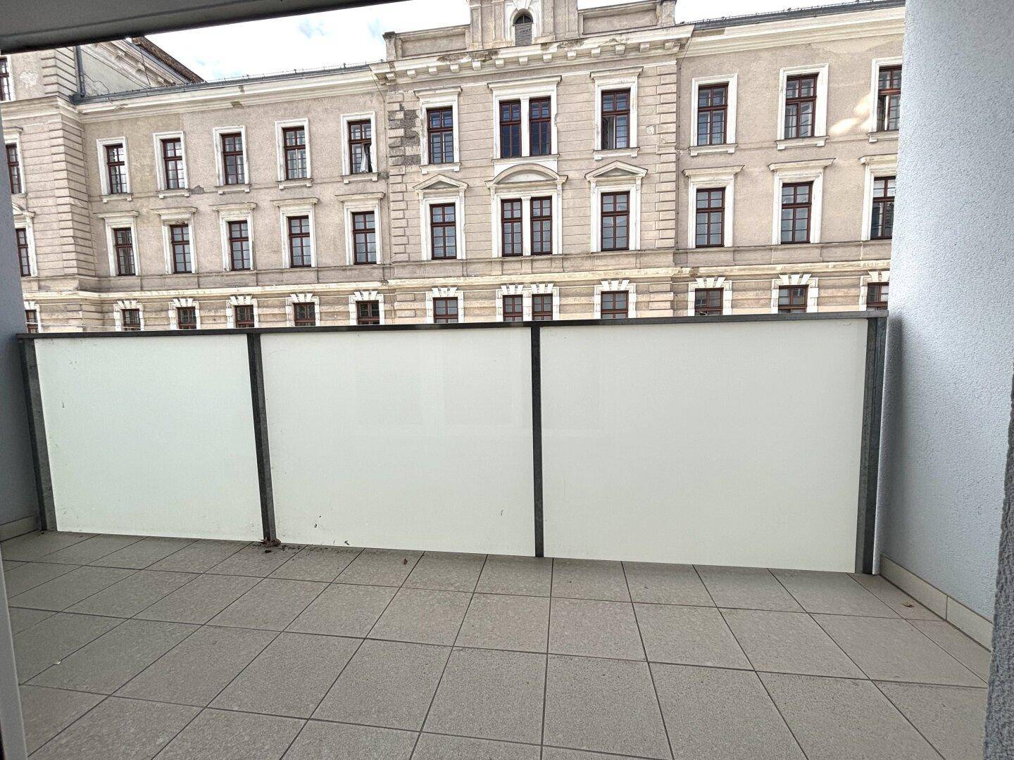 Balkon mit undurchsichtiger Brüstung und Blick auf ein historisches Gebäude.