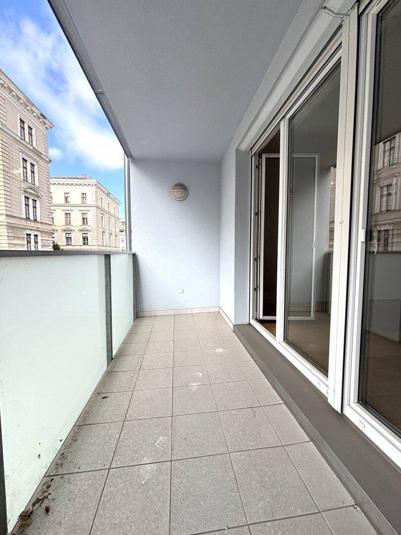 Leerer Balkon mit Fliesenboden und Blick auf die umliegenden Gebäude.