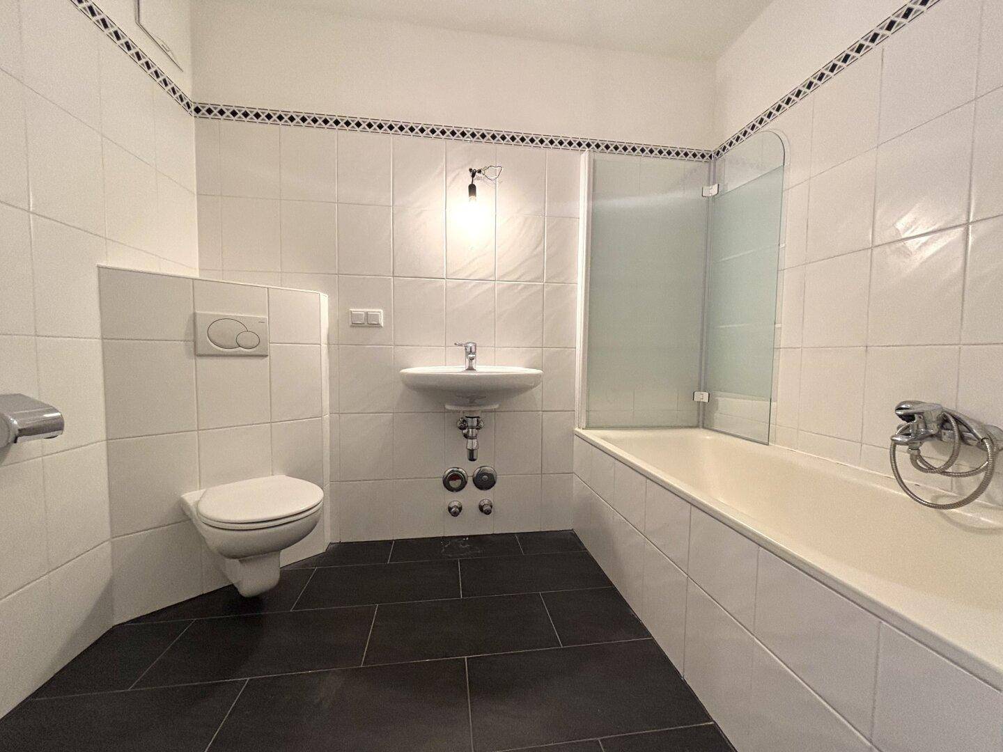 Badezimmer mit Badewanne, WC und weißen Fliesen.