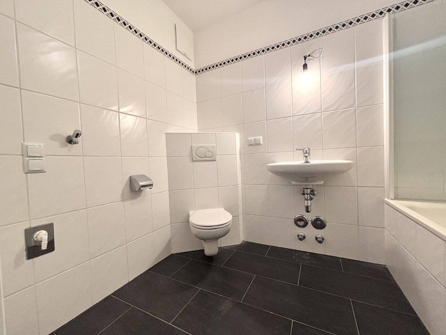 Badezimmer mit WC, Waschbecken und weißen Wandfliesen.
