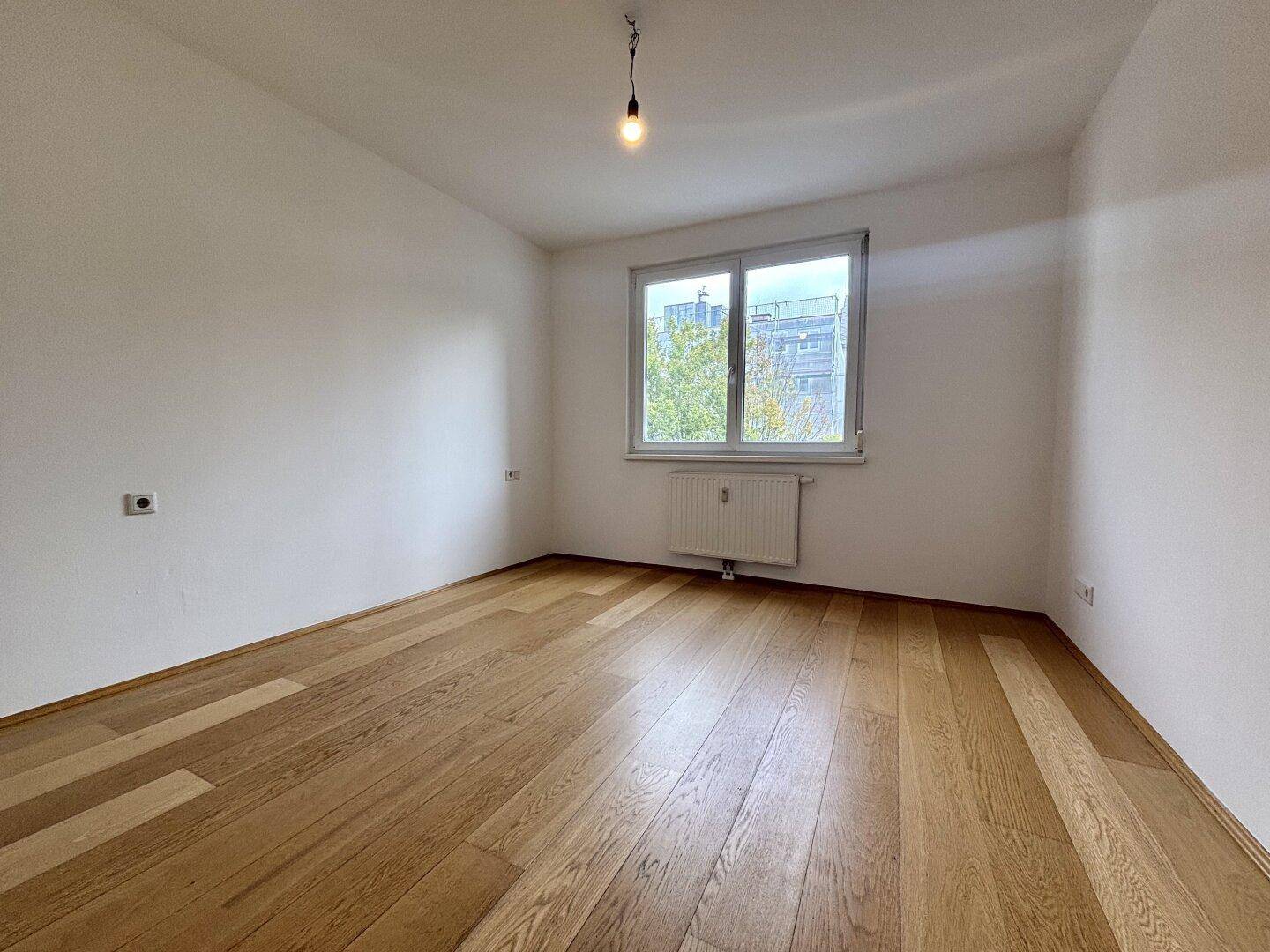 Leeres Schlafzimmer mit Holzboden und großem Fenster.