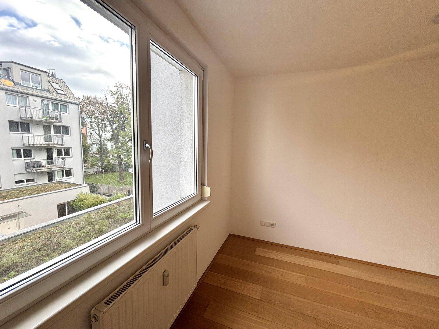 Kleiner Raum mit Holzboden und Fenster mit Blick ins Grüne.
