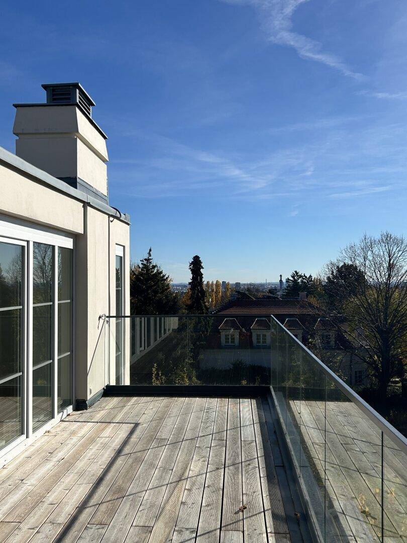 Holzterrasse mit Glasgeländer und Panoramablick über die Dächer und die grüne Umgebung.