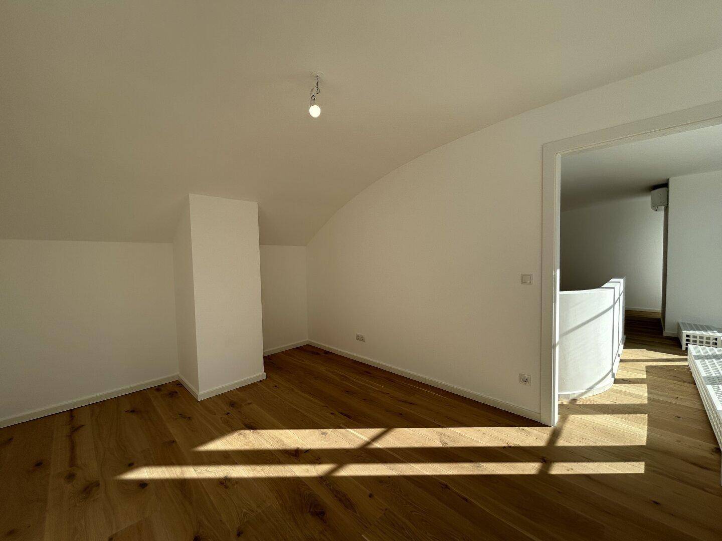 Heller Raum mit Holzboden und Dachschräge, der vielseitig genutzt werden kann.