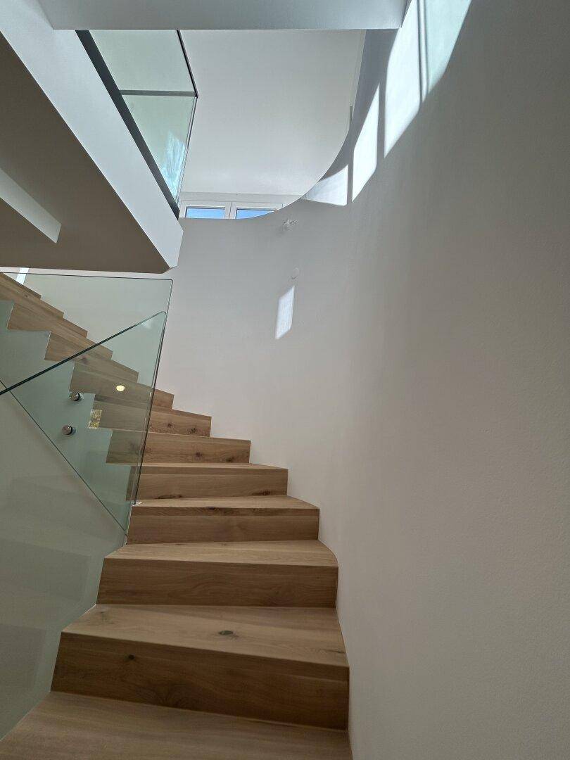 Moderne Holztreppe mit Glasgeländer, die die verschiedenen Ebenen des Hauses verbindet.