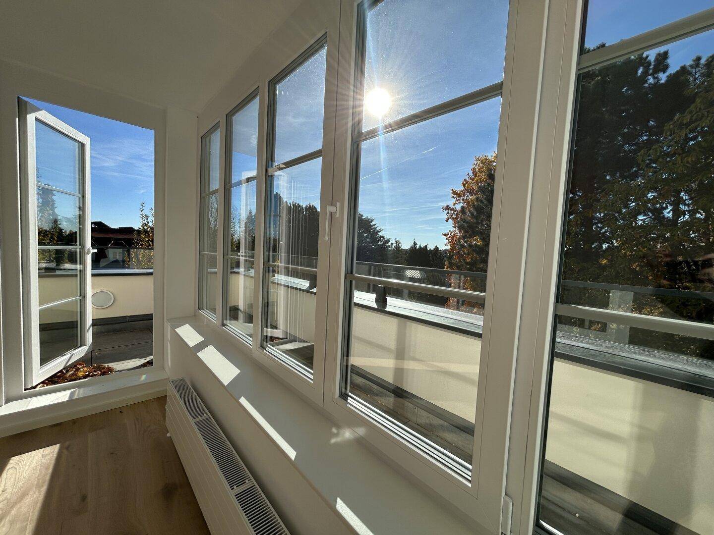 Sonniger Innenraum mit großen Fenstern, die viel Tageslicht hereinlassen und einen Ausblick bieten.
