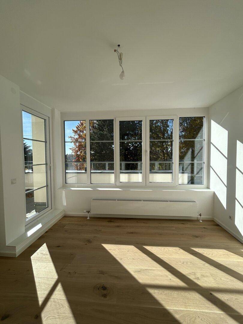 Lichtdurchfluteter Raum mit Holzboden und breiten Fenstern, die einen weiten Ausblick ermöglichen.
