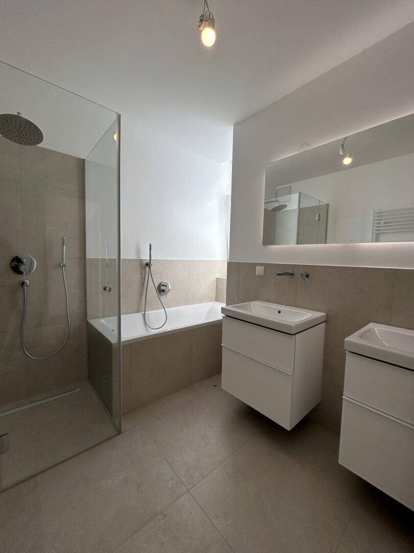 Modernes Badezimmer mit Badewanne, begehbarer Dusche und Doppelwaschbecken in hellen Fliesen.