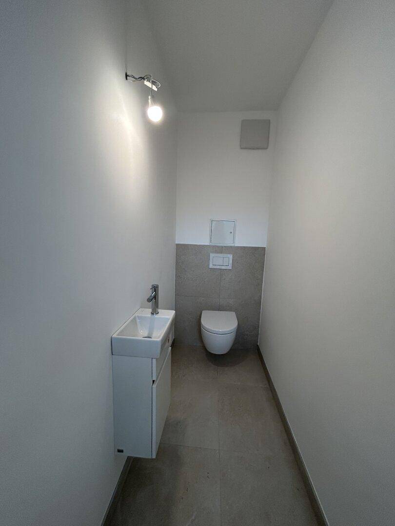 Kompaktes Gäste-WC mit Wand-WC und kleinem Waschbecken, modern gefliest und funktional.