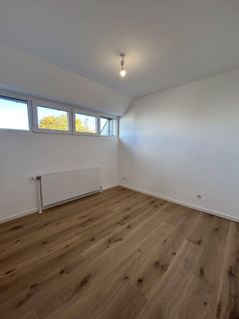 Modernes Zimmer mit Holzboden und Heizkörper, bereit für individuelle Gestaltung und Nutzung.