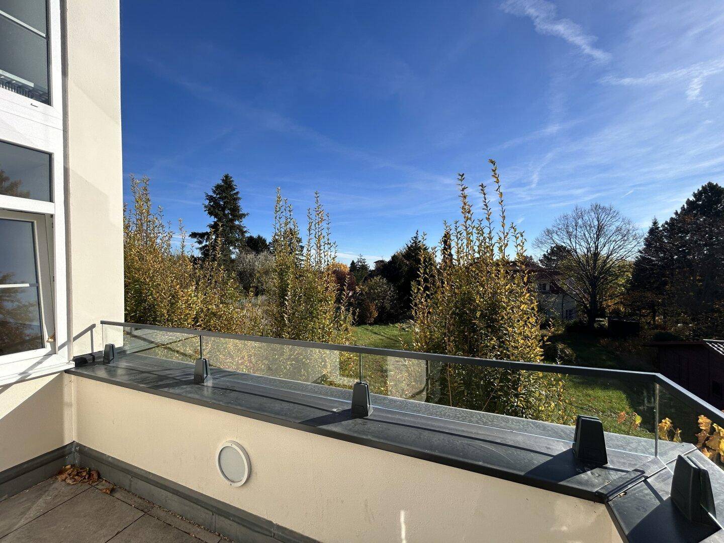 Kleiner Balkon mit Fliesenboden und Glasgeländer, bietet einen Blick ins Grüne.