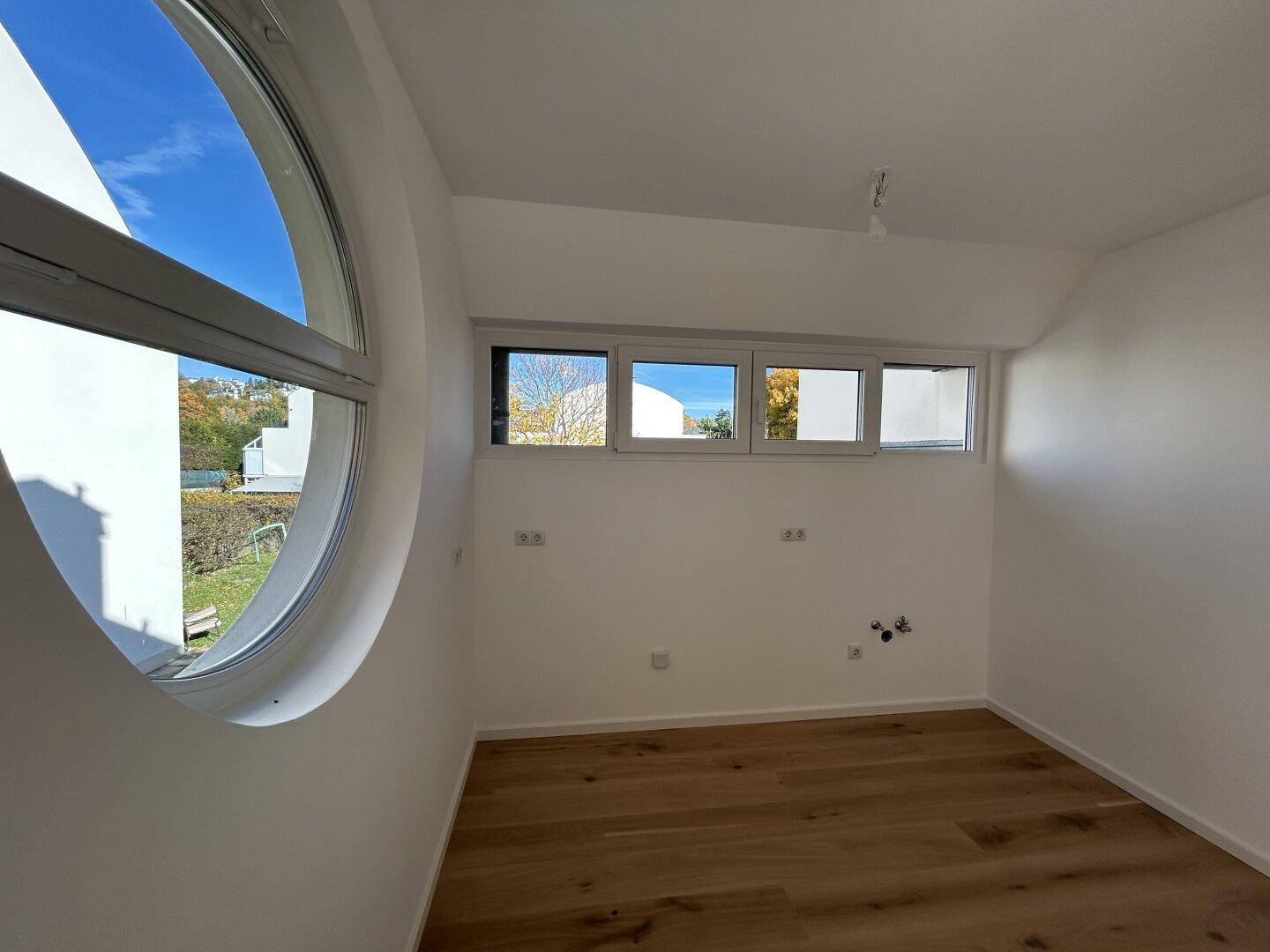 Geräumiges Zimmer mit markantem Rundfenster und Holzboden, ideal als Schlaf- oder Arbeitszimmer.