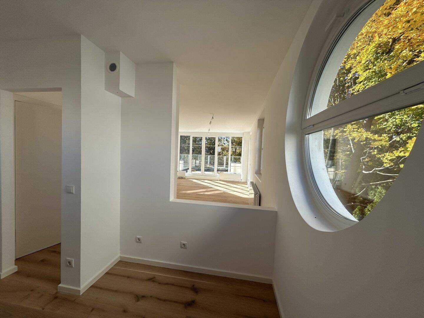 Offener Flurbereich mit Rundfenster und Blick in einen hellen Wohnraum mit großen Fenstern.