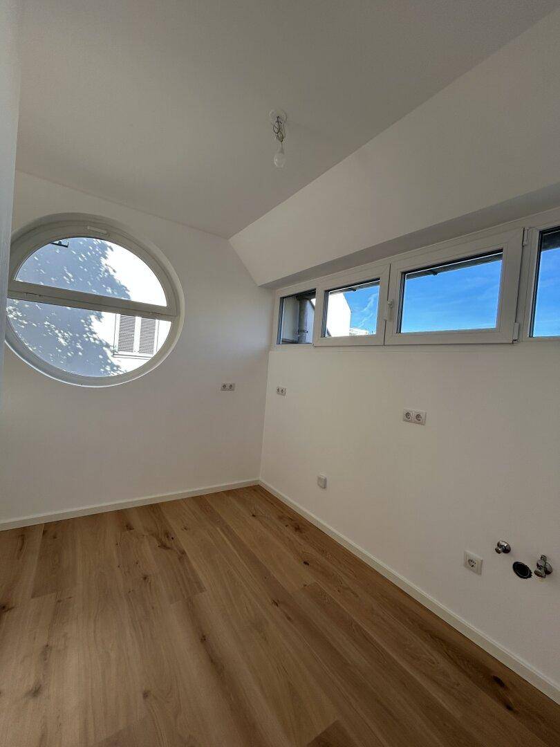 Helles Zimmer mit einzigartigem Rundfenster, Holzboden und weiteren Fenstern für viel Licht.