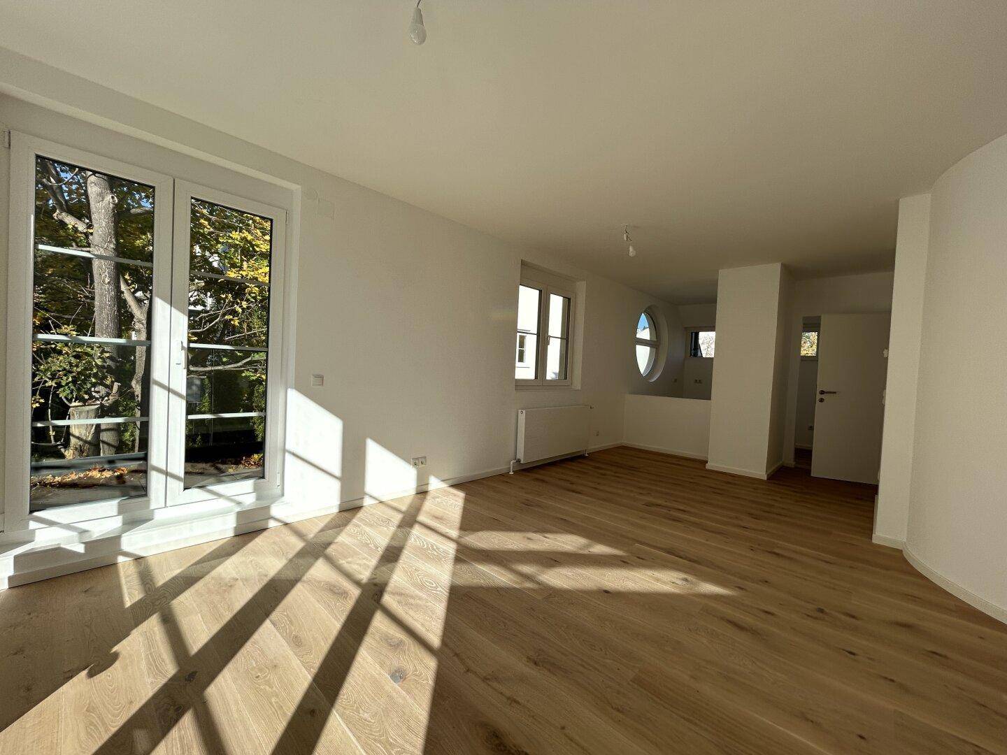 Heller, leerer Raum mit Holzboden und Fenstern, die viel Tageslicht hereinlassen.