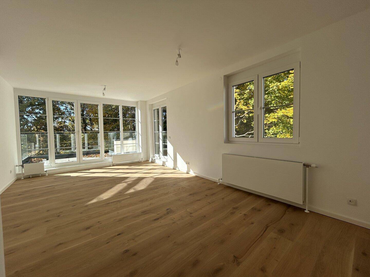 Geräumiger, heller Raum mit Holzboden und großen Fenstern, die viel Sonnenlicht hereinlassen.