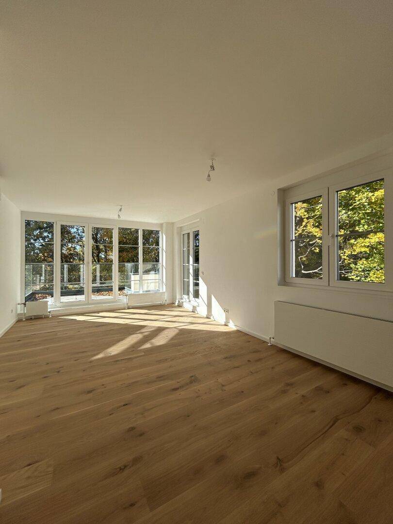Geräumiger, heller Raum mit Holzboden und großen Fenstern, die viel Sonnenlicht hereinlassen.