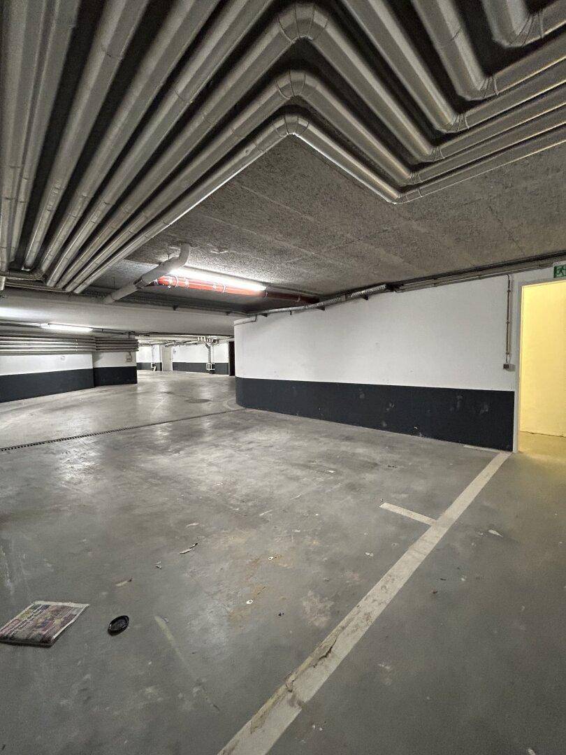 Geräumige Tiefgarage mit Betonboden, sichtbaren Rohren und ausreichend Parkflächen.