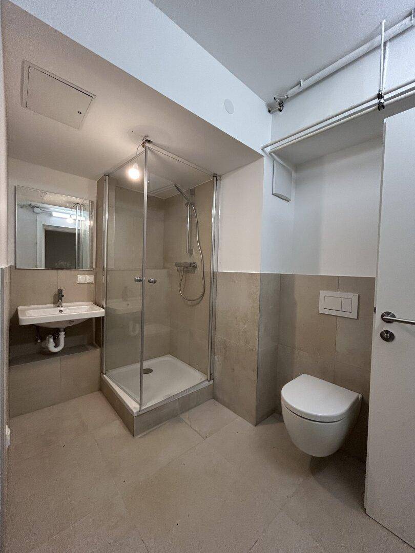 Funktionales Badezimmer mit Duschkabine, wandhängendem WC und kleinem Waschbecken.