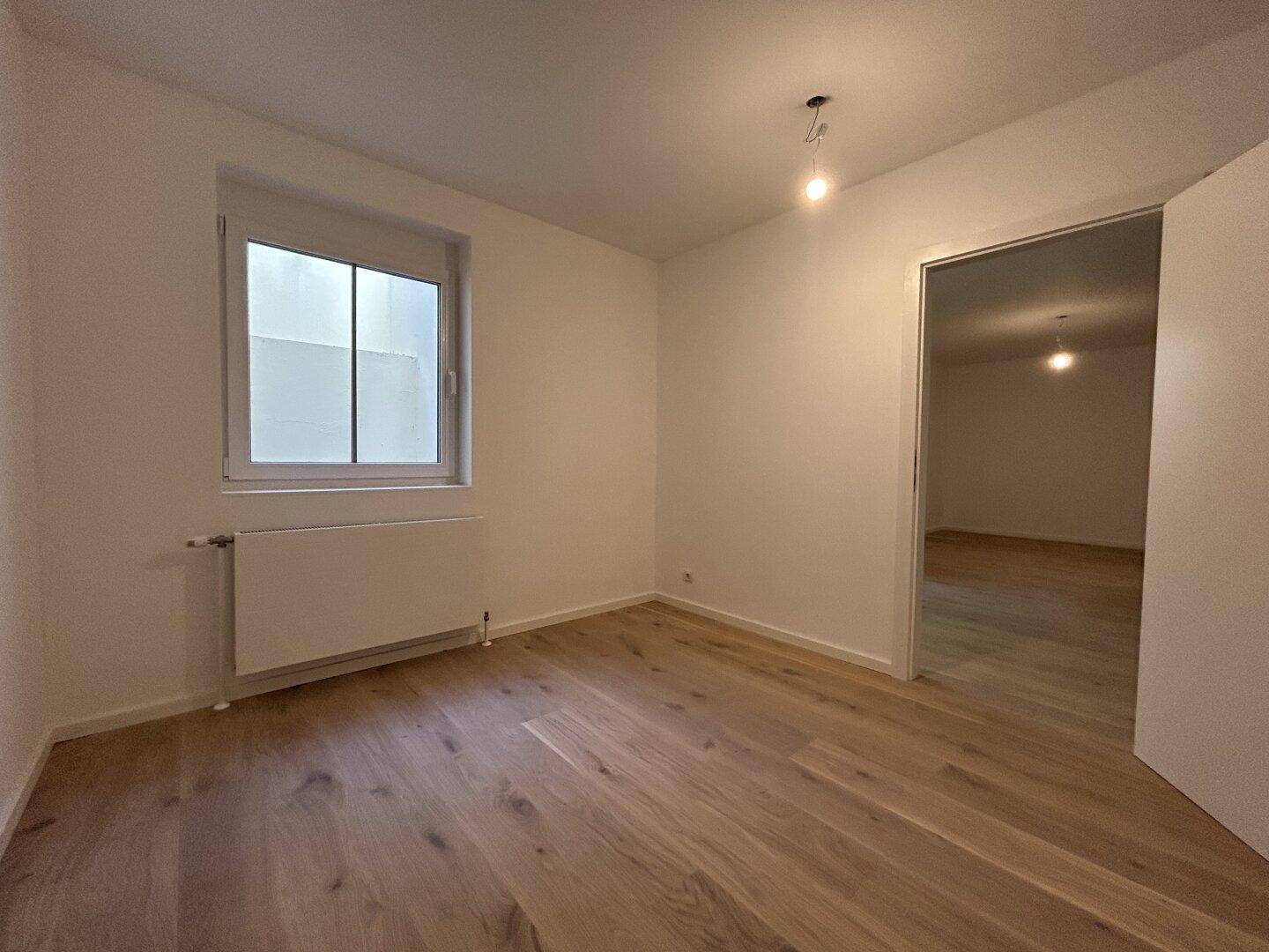 Leerer Raum mit Holzboden und Fenster, bereit zur individuellen Gestaltung.