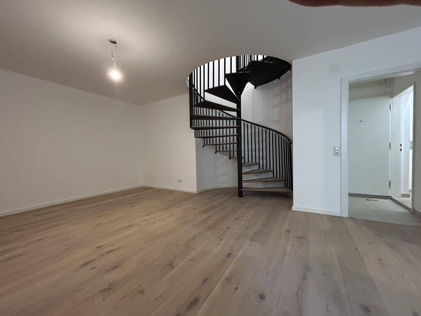 Geräumiger Wohnbereich mit hellem Holzfußboden und eleganter schwarzer Wendeltreppe.