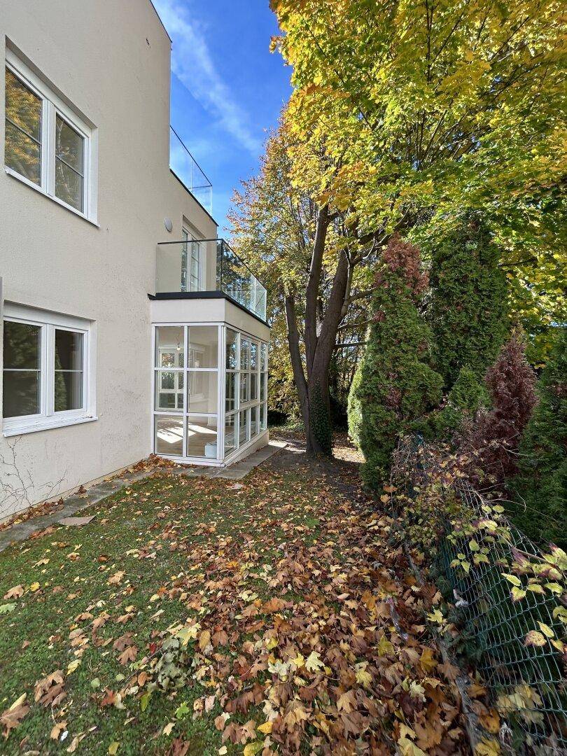 Seitenansicht des Gebäudes mit verglastem Anbau und umgebender Natur im Herbst.