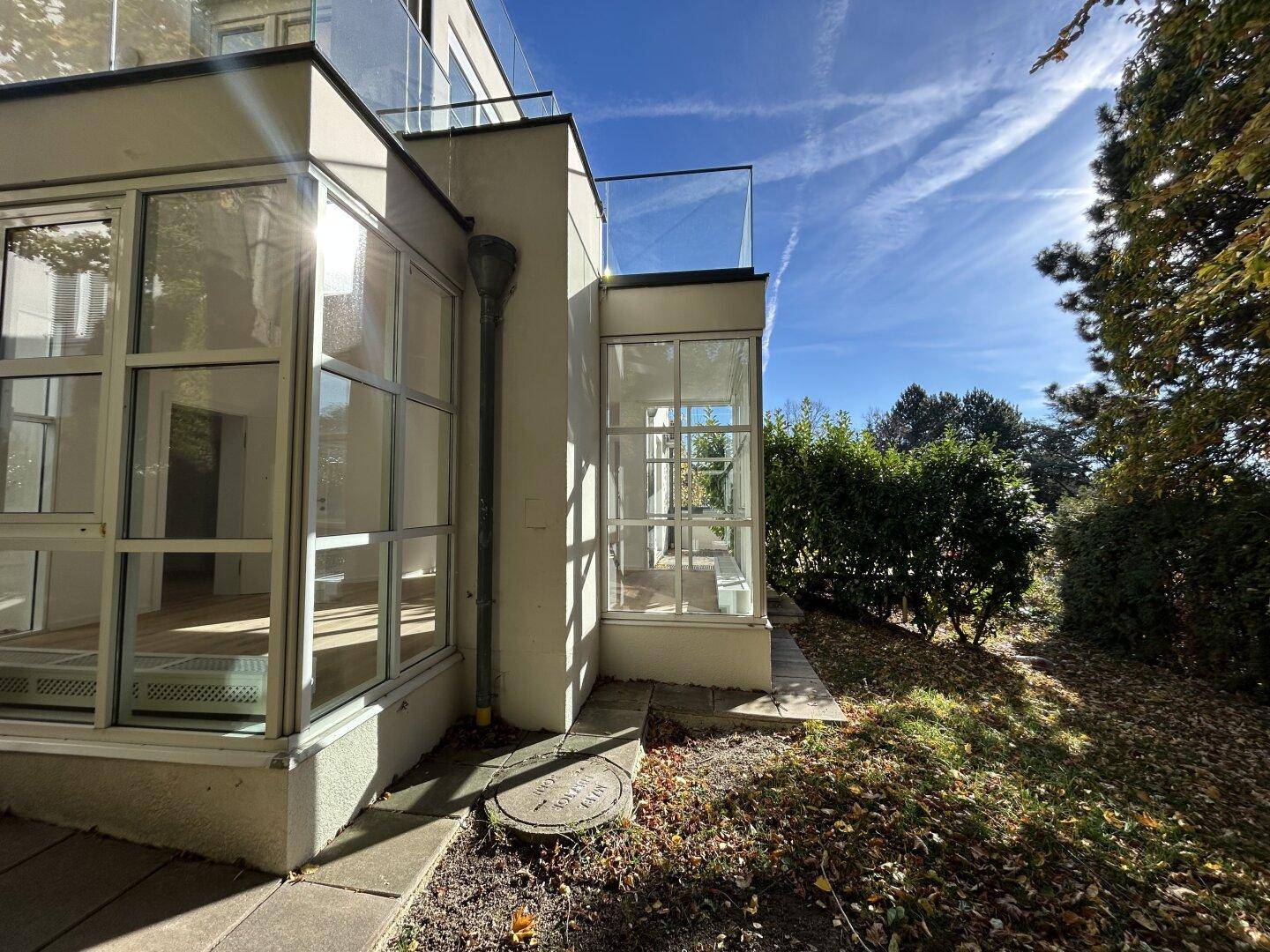 Moderne Gebäudefassade mit großen Glasflächen und umgebender Bepflanzung.