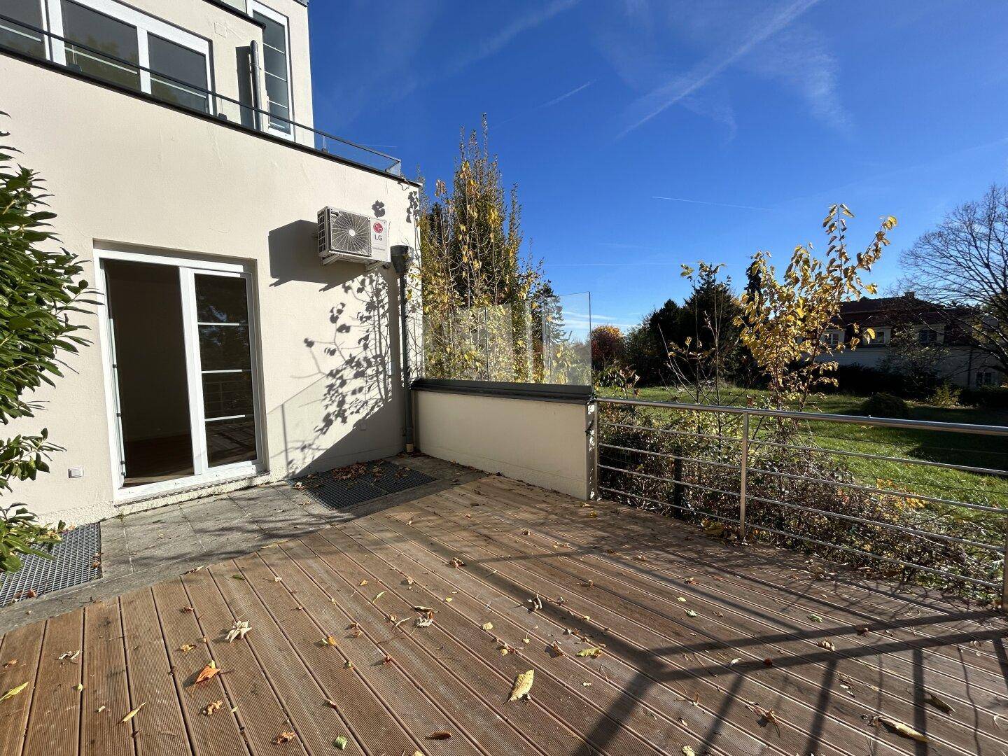 Sonnige Holzterrasse mit Glasbrüstung und weitem Blick in die Natur.
