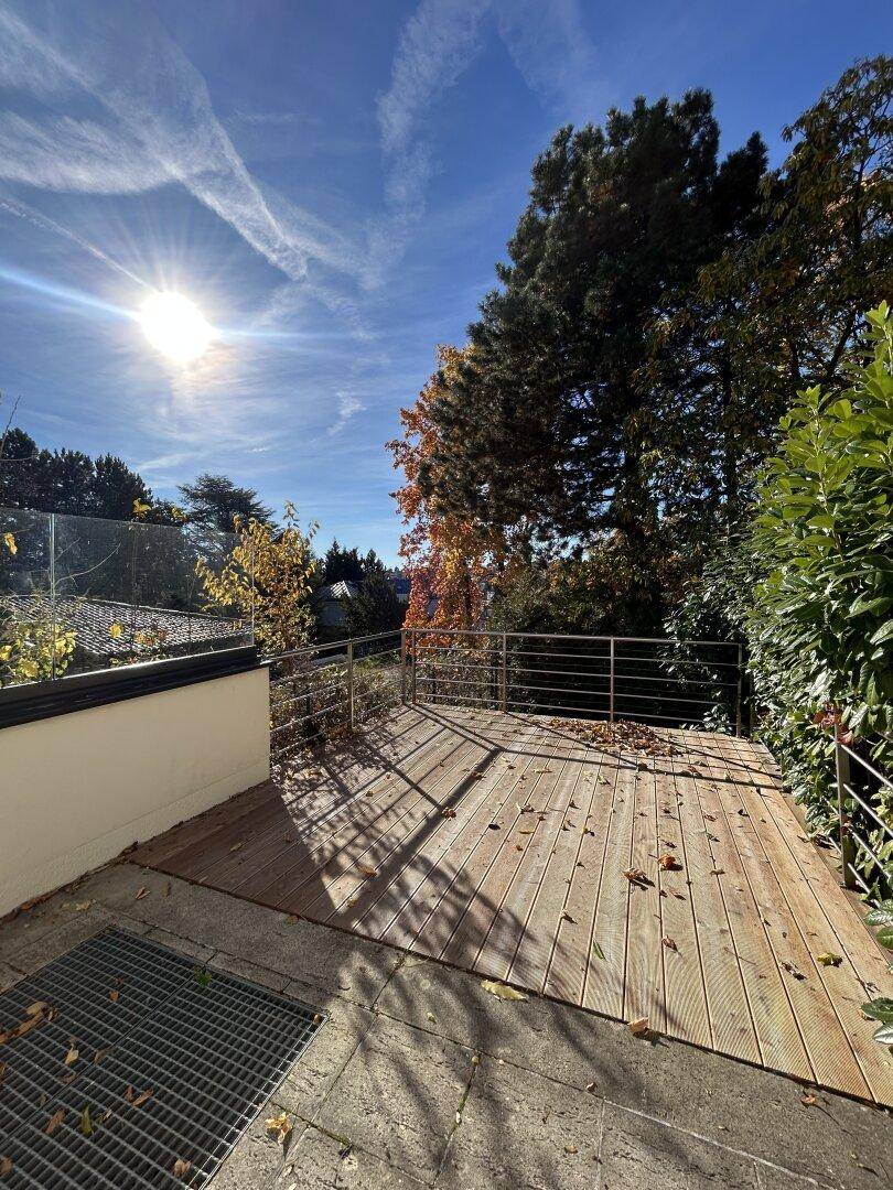 Holzterrasse unter blauem Himmel mit viel Sonnenlicht und umgebenden Bäumen.