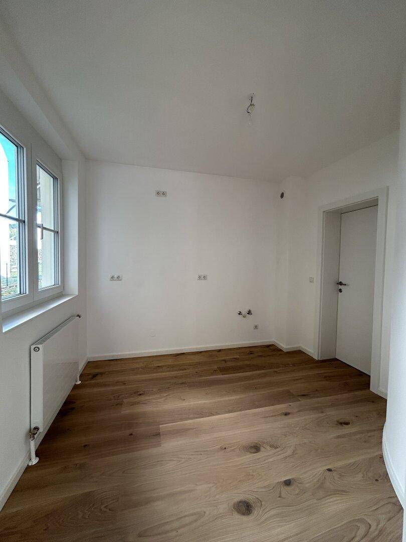 Leerer Raum mit Holzboden, Fenster und vorbereiteten Anschlüssen.