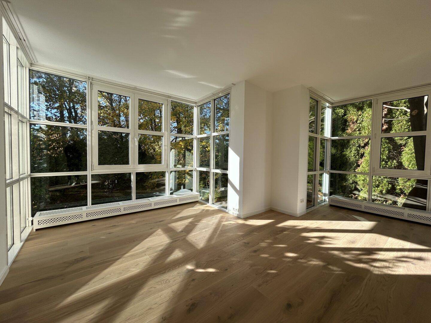Geräumiges Wohnzimmer mit großen Fenstern, Holzboden und viel Tageslicht.