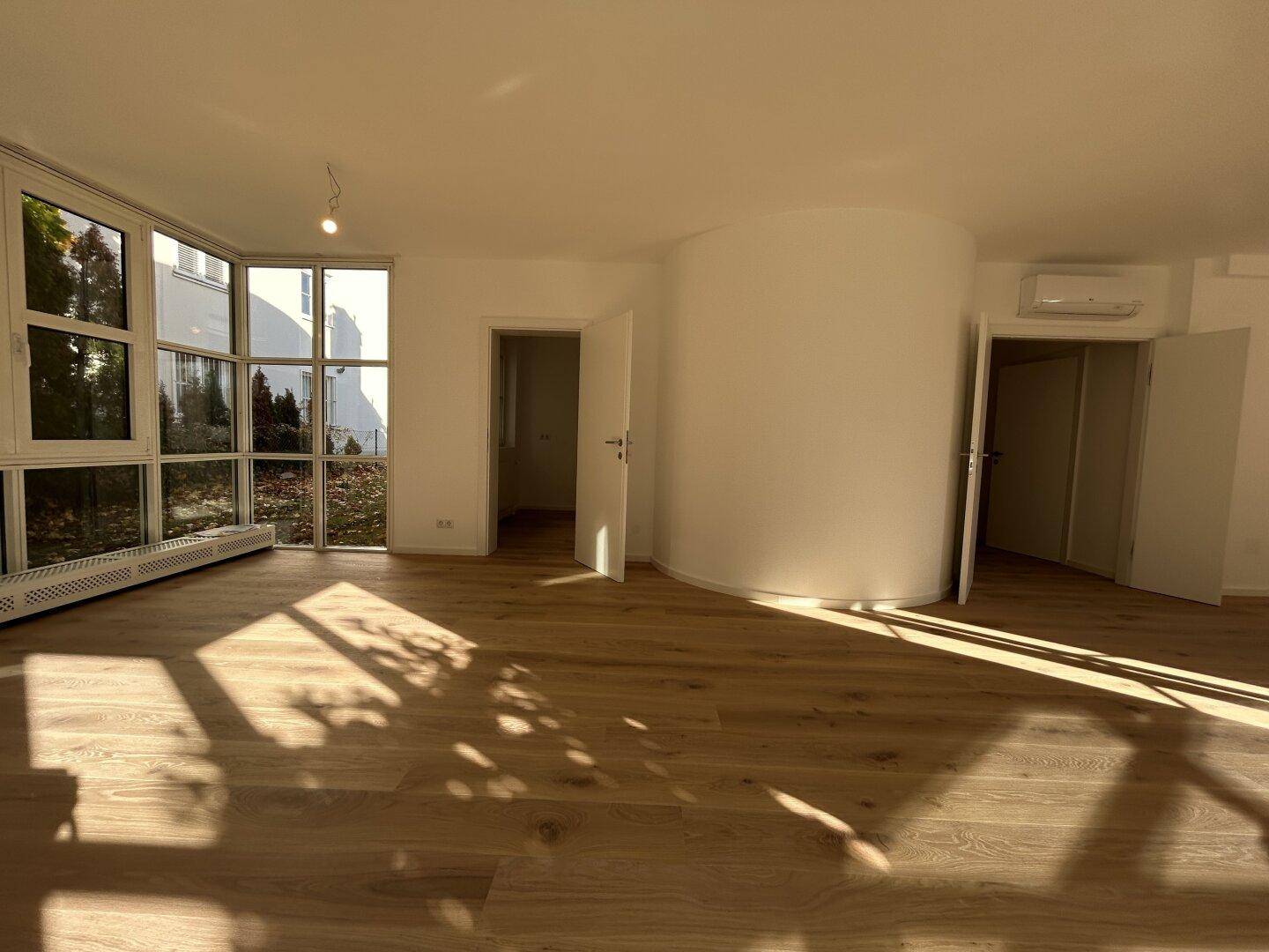 Heller Wohnbereich mit Holzboden, großen Fenstern und viel Sonnenlicht.