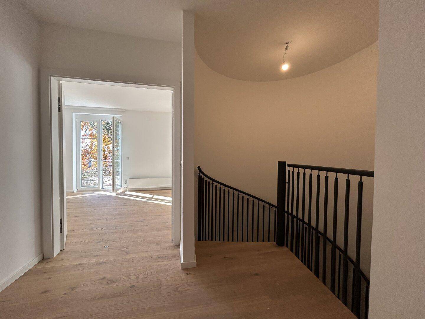 Heller Flur mit Holzfußboden und Zugang zu einem Zimmer mit Balkon.