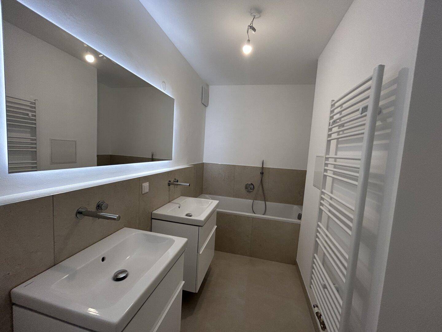 Modernes Badezimmer mit Doppelwaschbecken, Badewanne und beleuchtetem Spiegel.