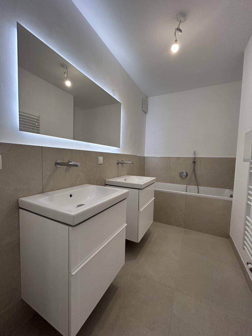 Elegantes Badezimmer mit zwei modernen Waschtischen und großem, hinterleuchtetem Spiegel.