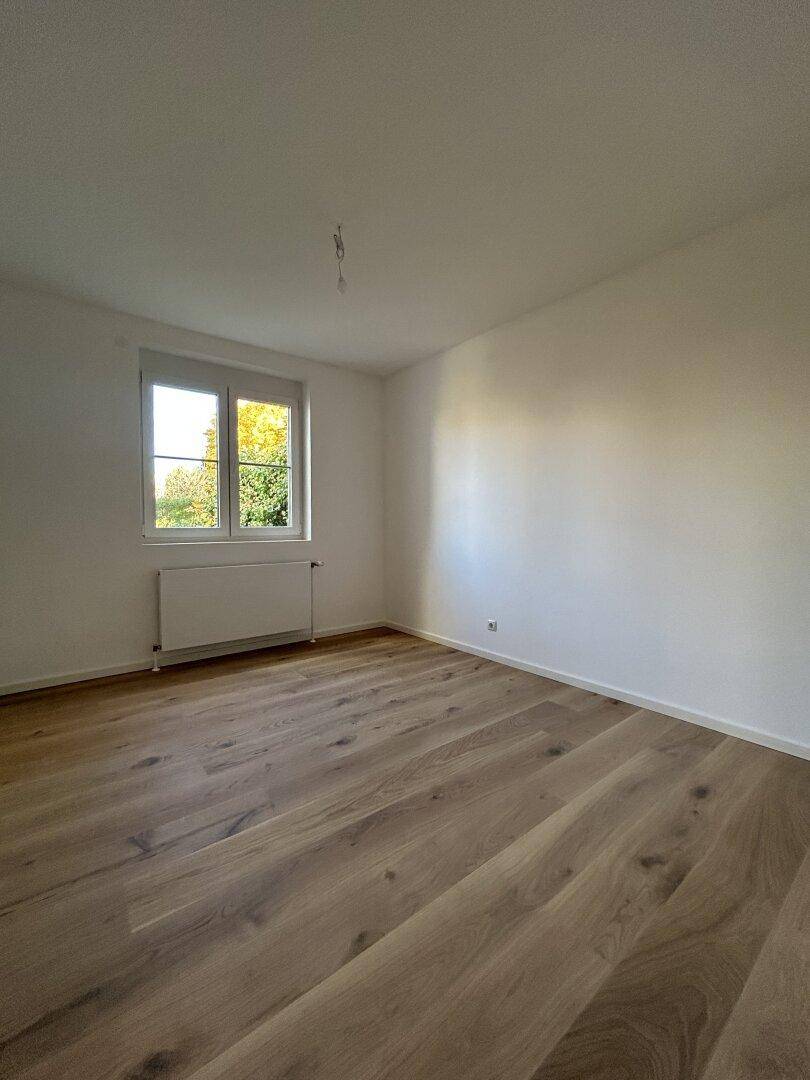 Helles Schlafzimmer mit Holzboden und großem Fenster, ideal für natürliche Belichtung.