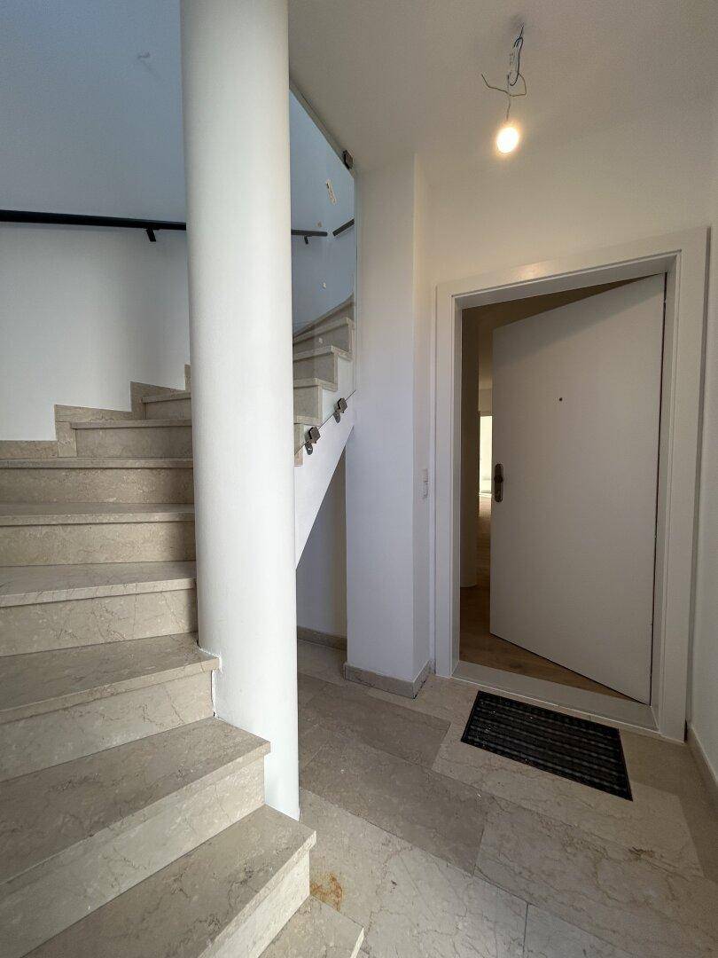 Eingangsbereich mit Steintreppe und heller Eingangstür, die zu den oberen Etagen führt.