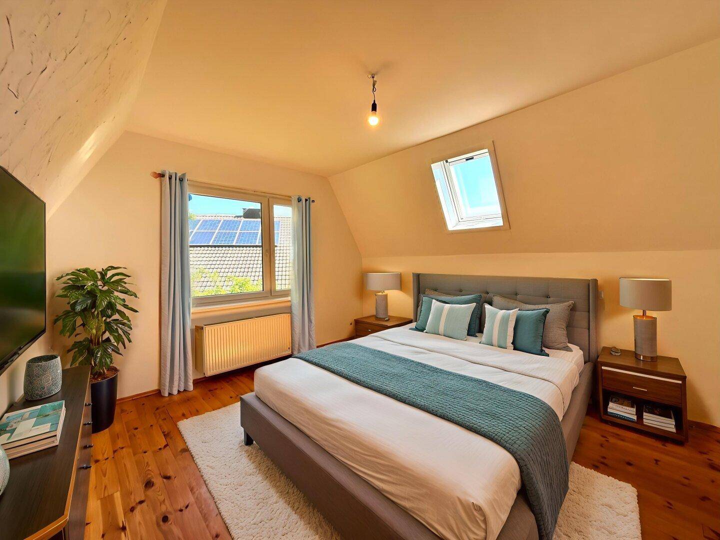 Gemütliches Schlafzimmer im Dachgeschoss mit Holzboden, Dachfenster und Blick auf Solaranlagen.