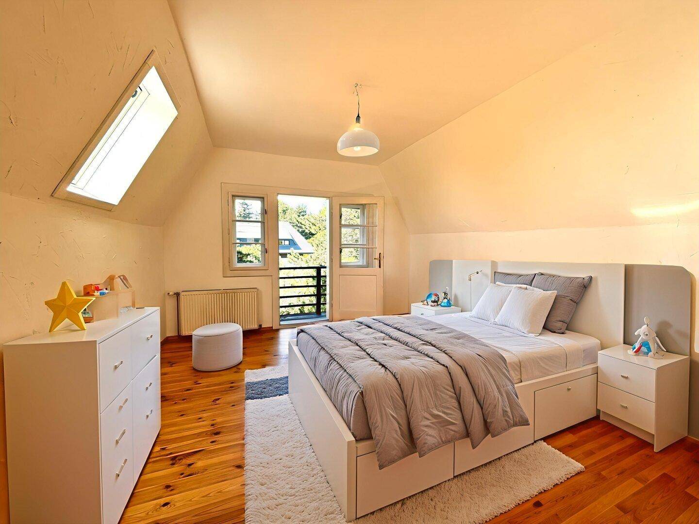 Kinderzimmer im Dachgeschoss mit Holzboden, Dachfenster und Zugang zu einem französischen Balkon.