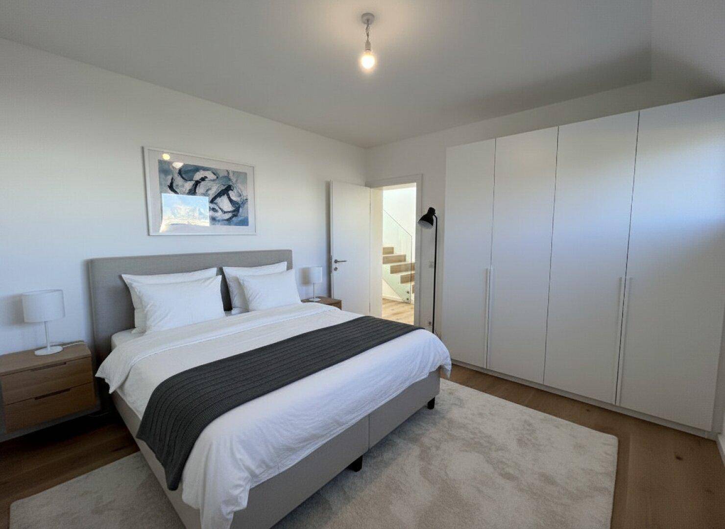 Helles Schlafzimmer mit Holzboden, großem Kleiderschrank und Zugang zu einem weiteren Bereich.