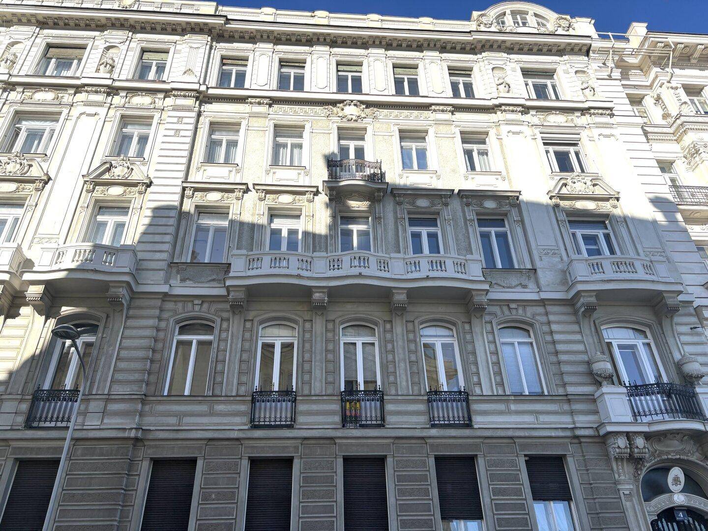 Detailansicht einer historischen Fassade mit verzierten Balkonen und vielen Fenstern.