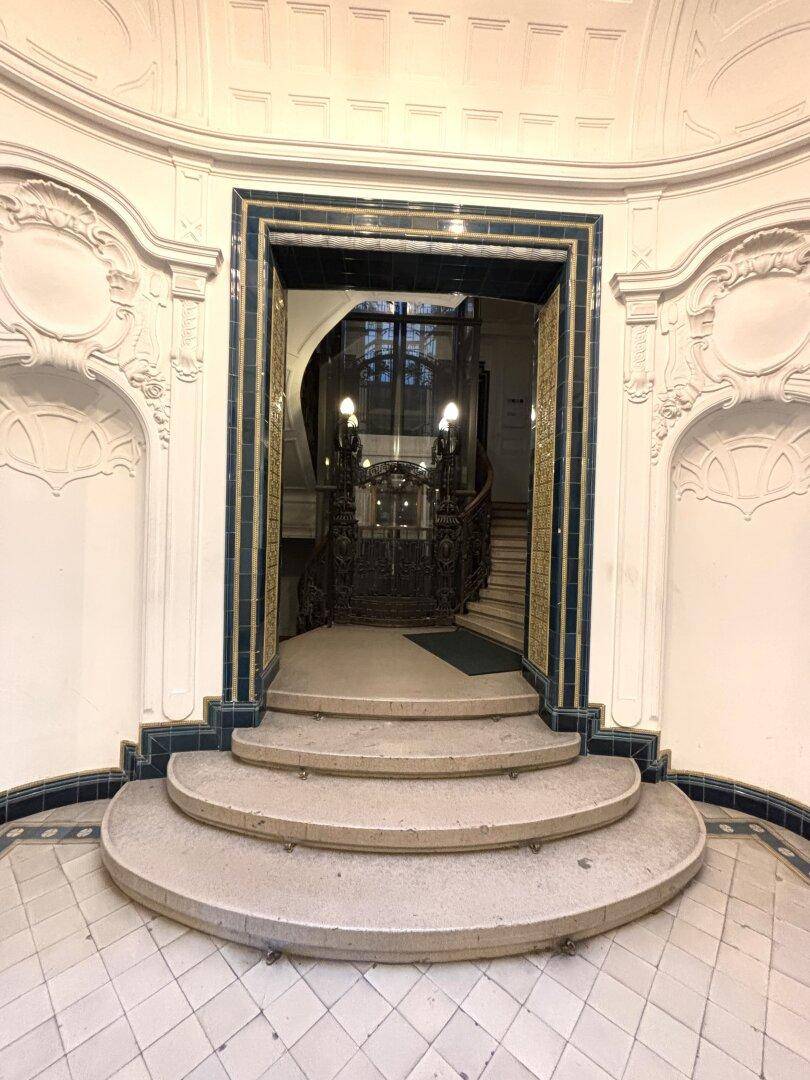 Historischer Eingangsbereich mit geschwungener Steintreppe und kunstvollen Verzierungen.