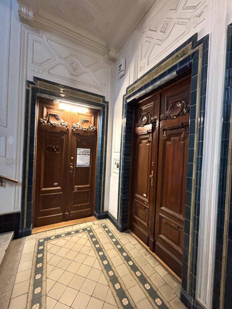 Historischer Flur mit verzierten Holztüren, Fliesenboden und kunstvollen Wanddetails.