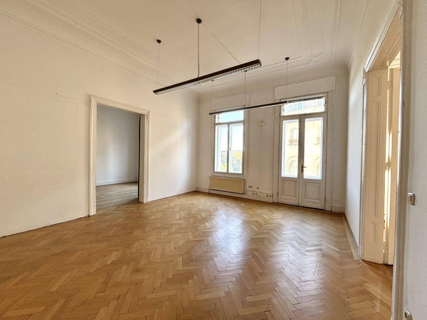 Heller, leerer Büroraum mit Parkettboden, hohen Fenstern und klassischer Stuckverzierung an der Decke.