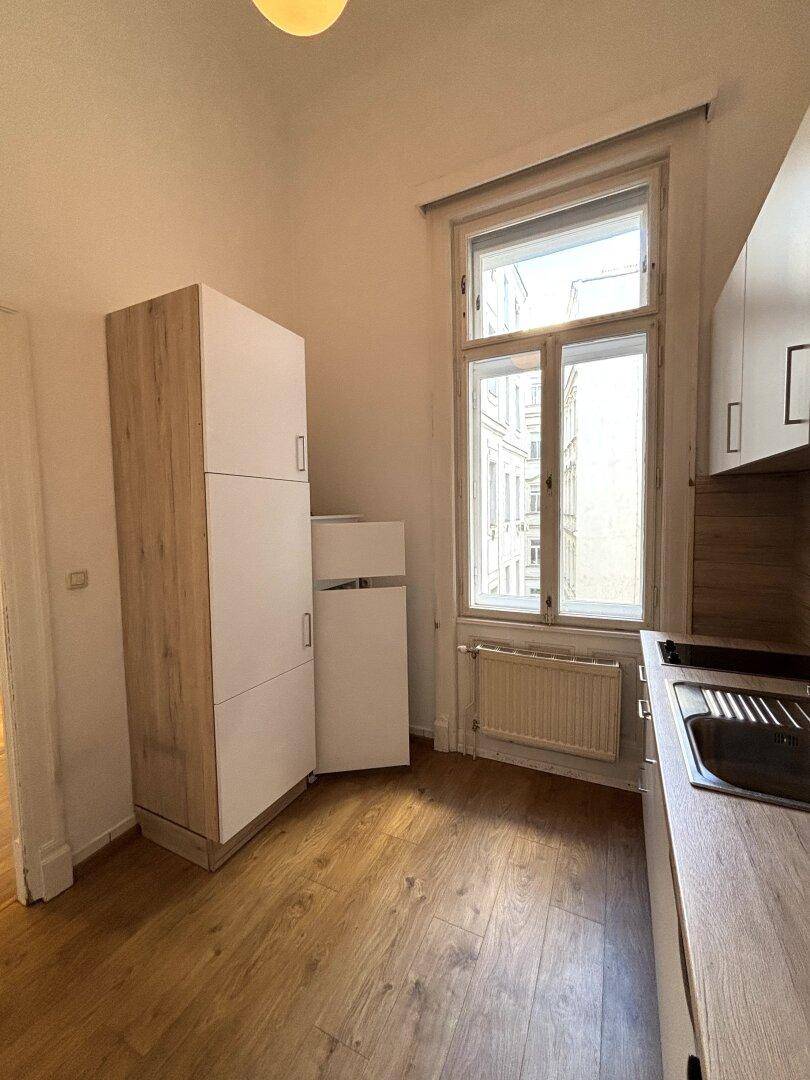 Kompakte Küche mit weißen und holzfarbenen Schränken, Fenster und Spülbecken.