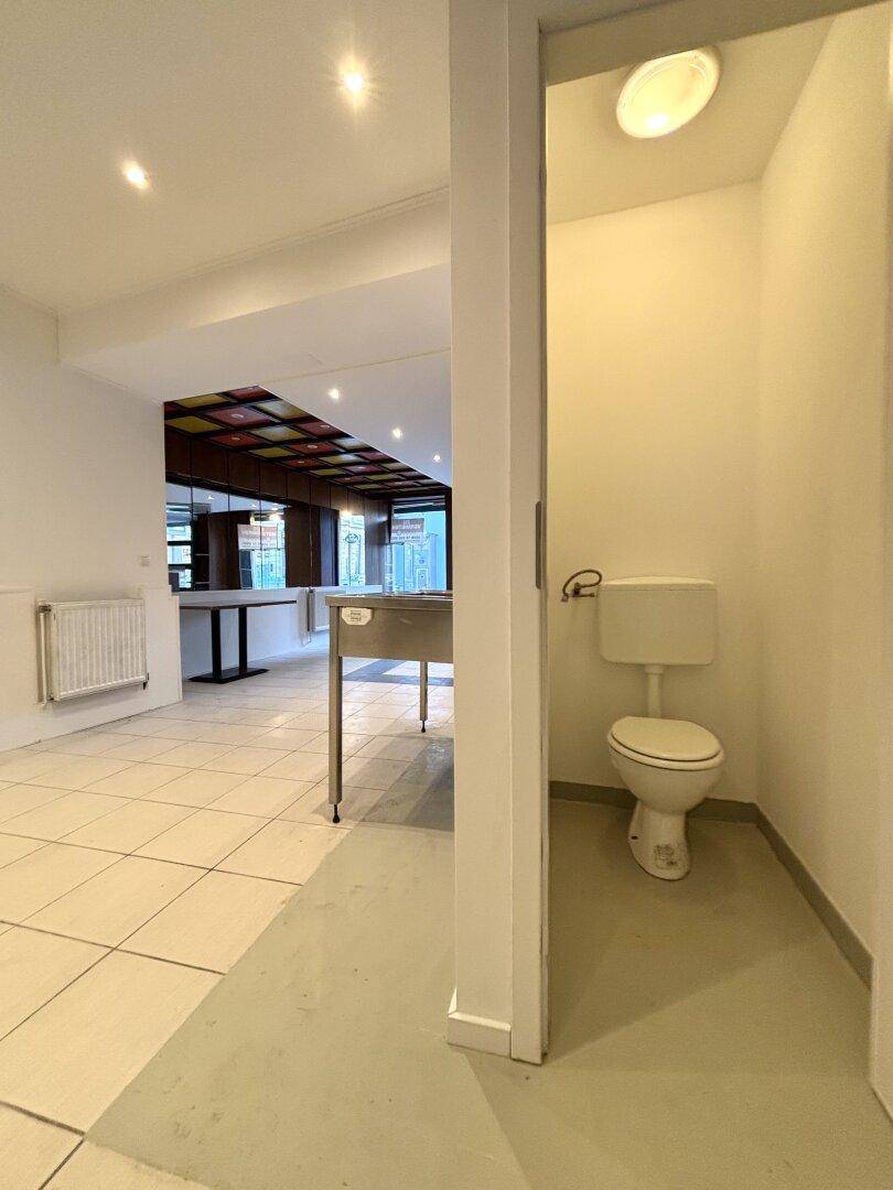 Einfache Toilette mit weißer Keramik und einem Deckenlicht, angrenzend an den Gewerberaum.