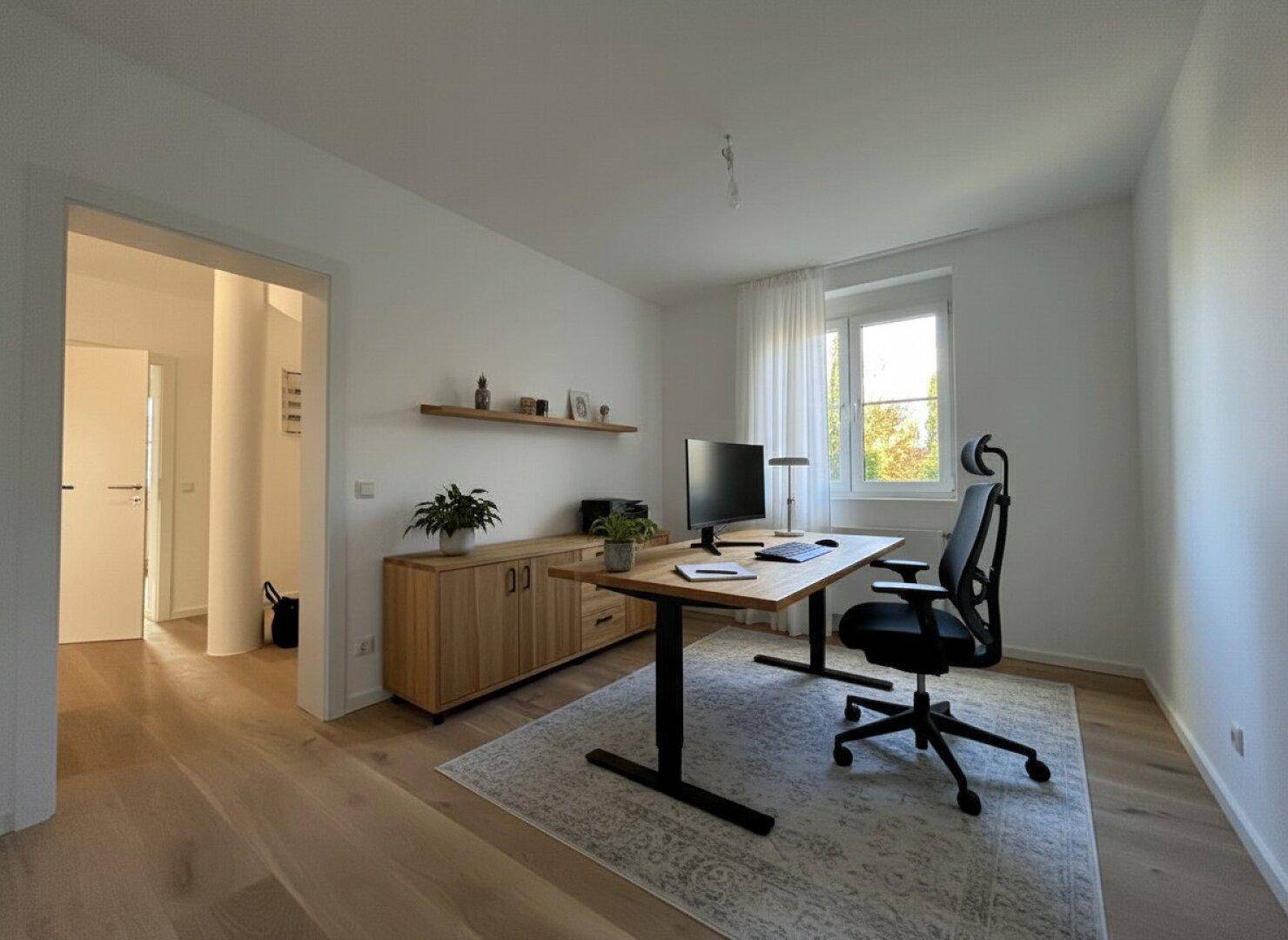 Helles Arbeitszimmer mit Holzboden, Schreibtisch und Blick ins Grüne.