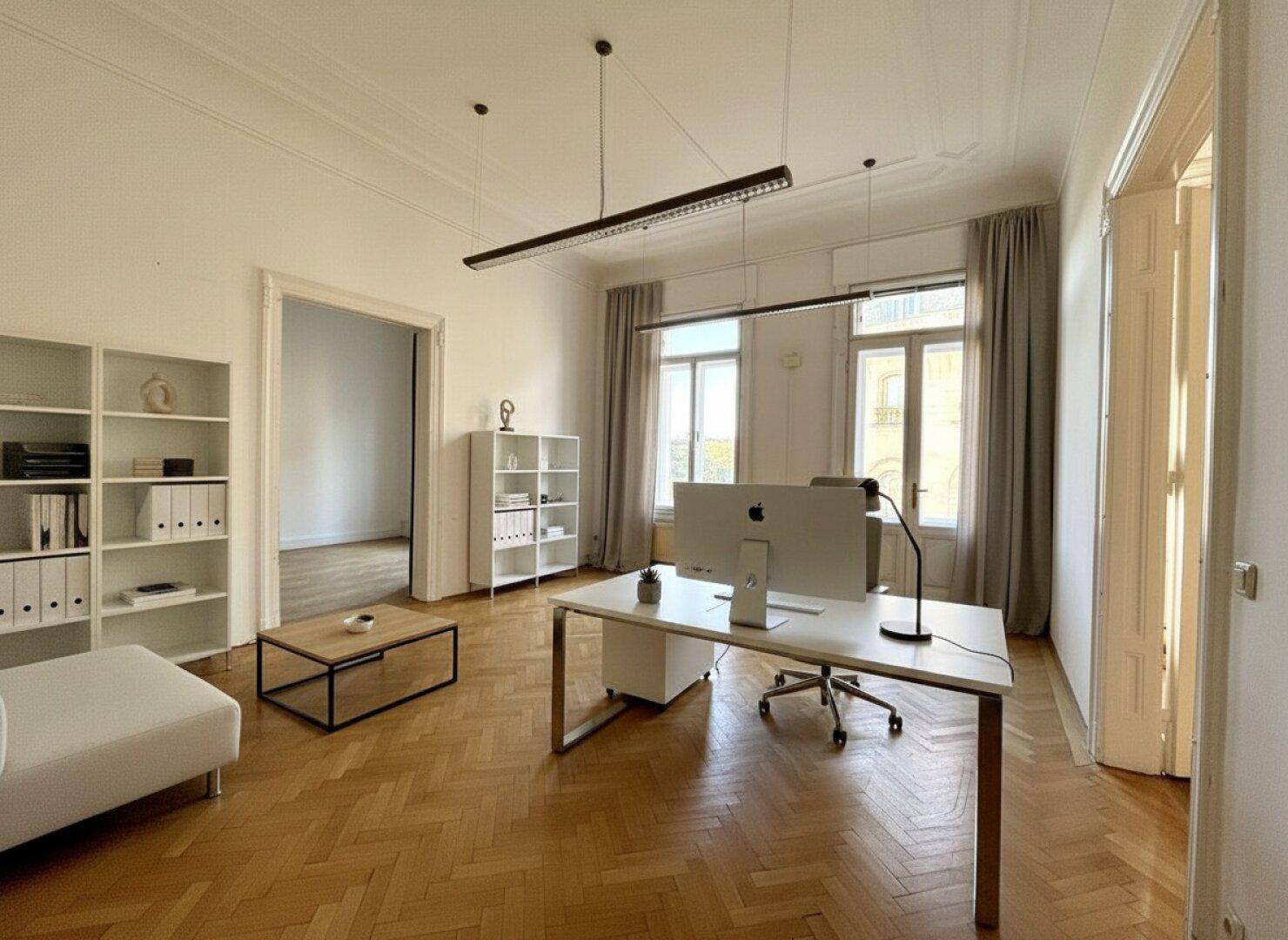 Helles Einzelbüro mit Schreibtisch, Regalen und bequemer Sitzgelegenheit, ausgestattet mit Parkettboden.