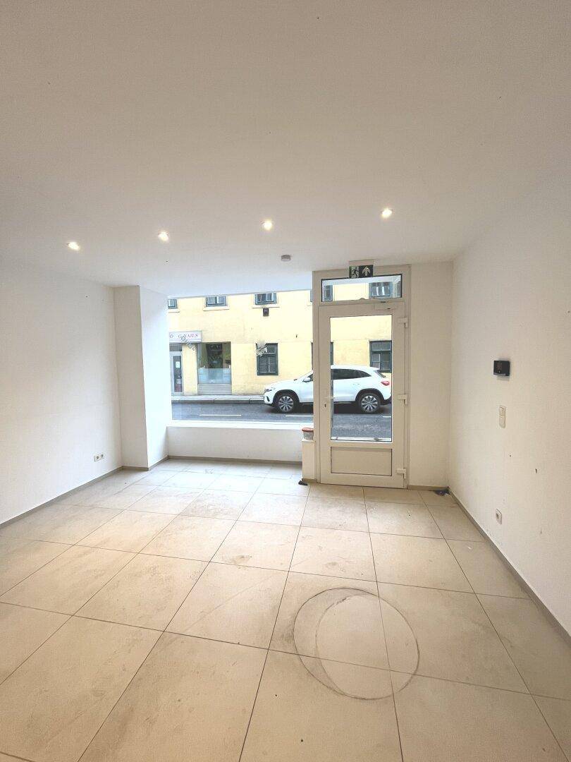 Unmöblierter Ladenbereich mit Fliesenboden und breiter Fensterfront zur Straße.